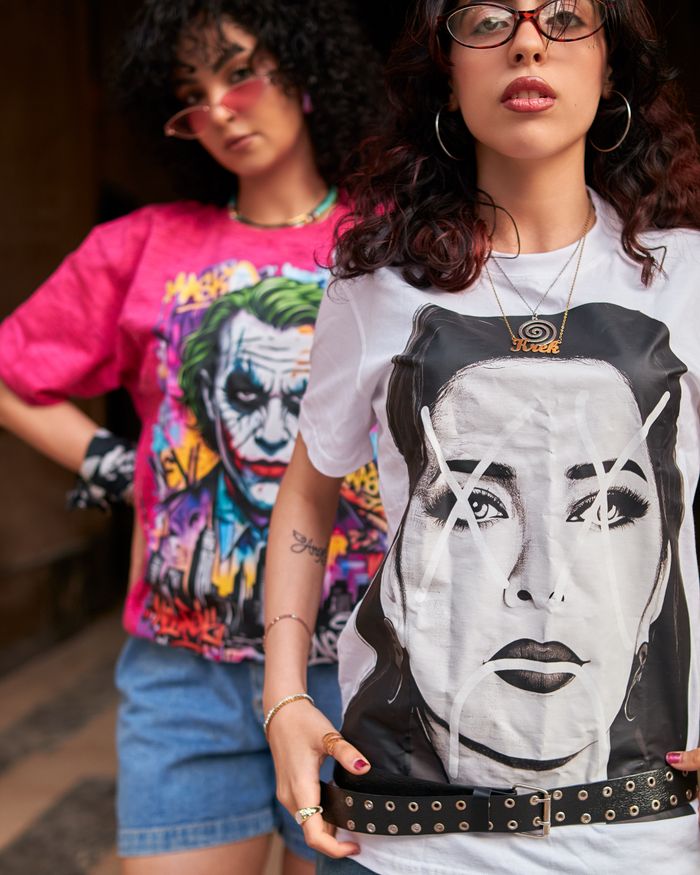 Two stylish women in graphic tees pose confidently outdoors, showcasing vibrant art.